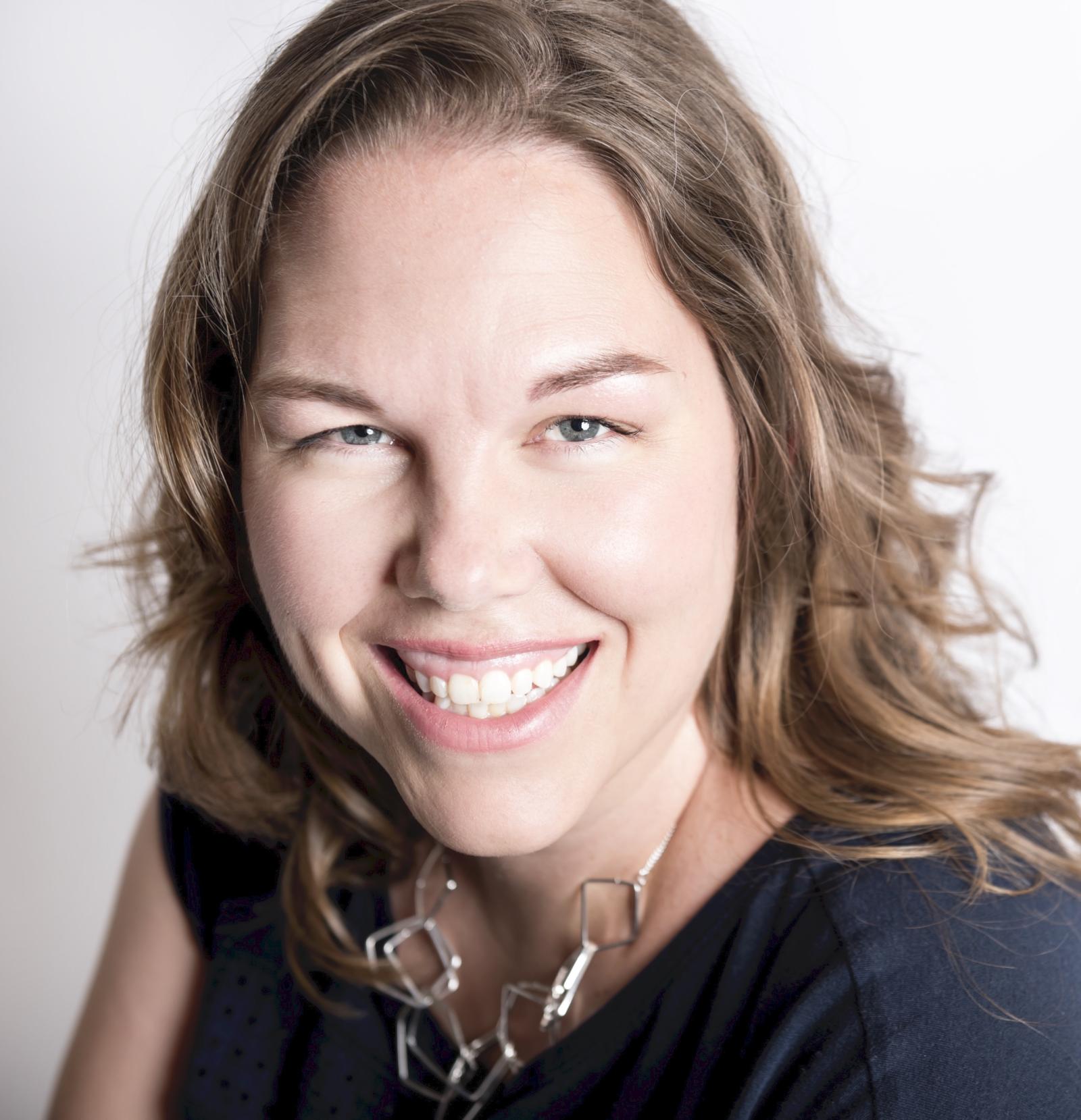 Photo of Amy Kristin Sanders, a white woman with dark wavy hair, smiling and looking at the camera. She is wearing a black shirt and silver necklace.